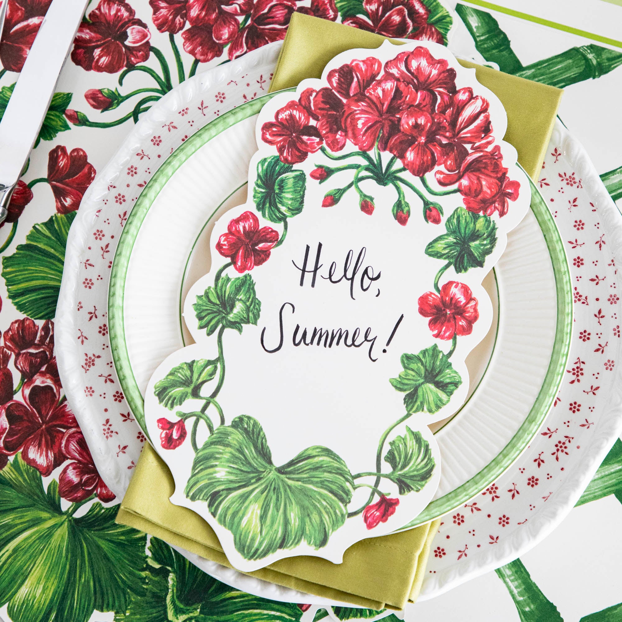A Geranium Table Accent with &quot;Hello Summer!&quot; written on it resting on the plate of an elegant place setting.