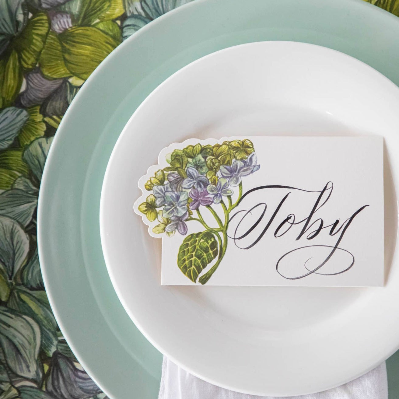 Hester &amp; Cook Hydrangea place cards adorned with multicolored blooms placed on a plate.