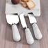A Zodax Marble Set of 3 Cheese Knives with white marble handles on a wooden table.