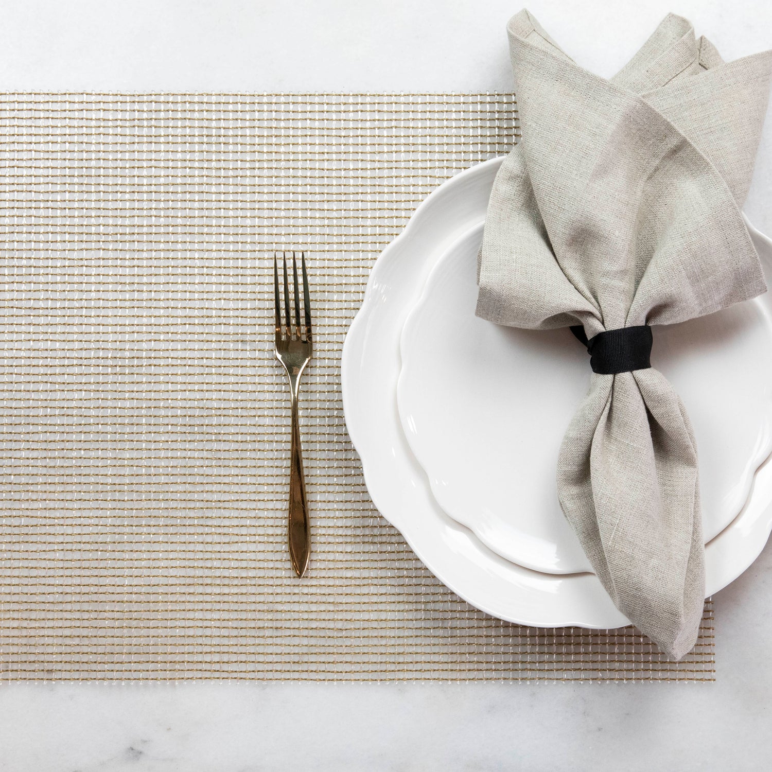 A neatly arranged table setting with a plate, folded napkin, and a fork on a Chilewich Lattice Table Mat.
