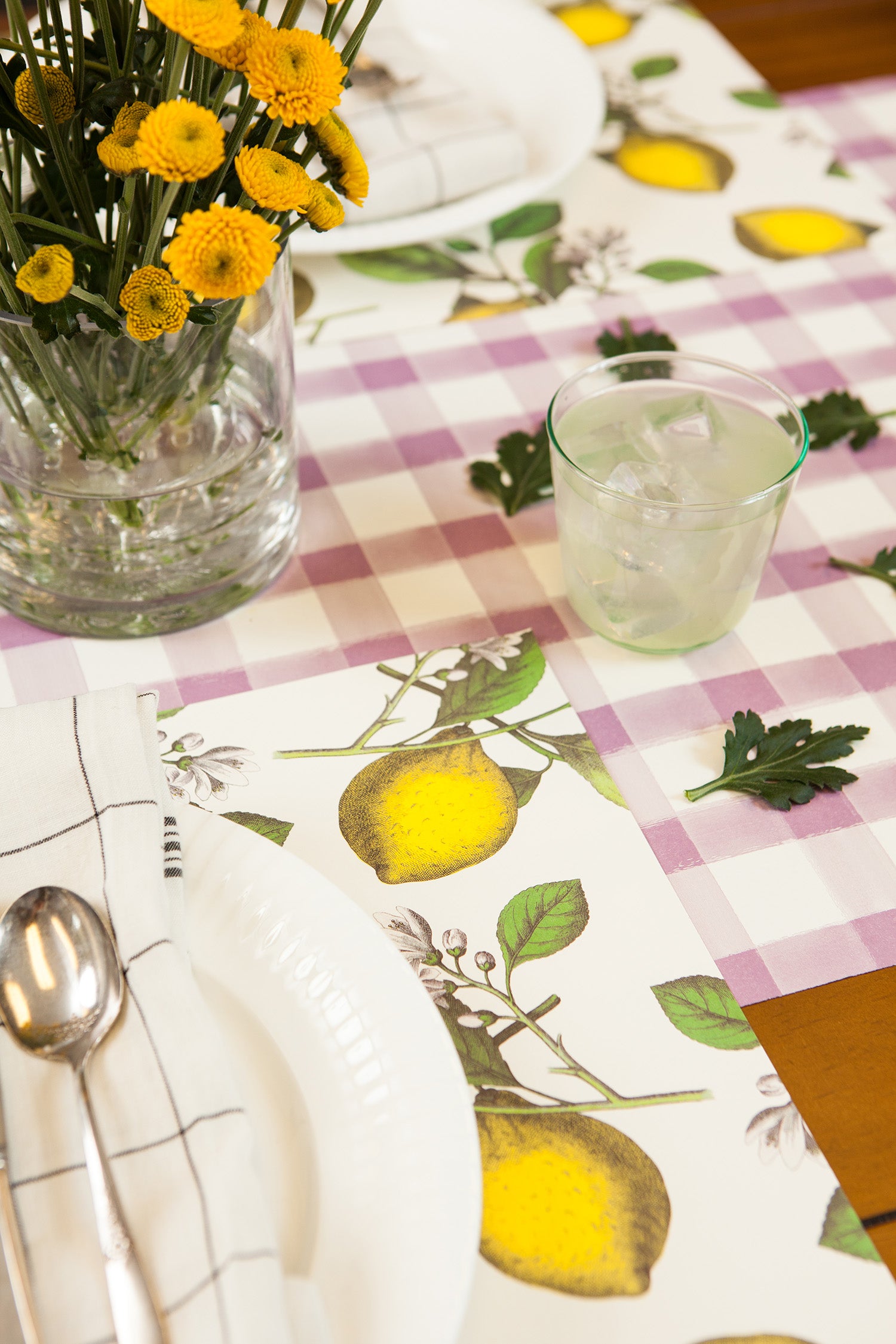 A table setting with flower decorations and lemons, featuring the Lilac Painted Check Runner by Hester &amp; Cook, perfect for entertaining.