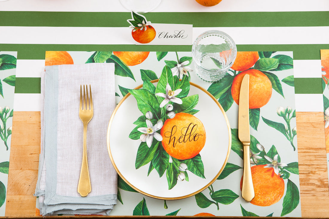 A table setting with Orange Orchard Placemats by Hester &amp; Cook on a citrus-themed tablecloth.