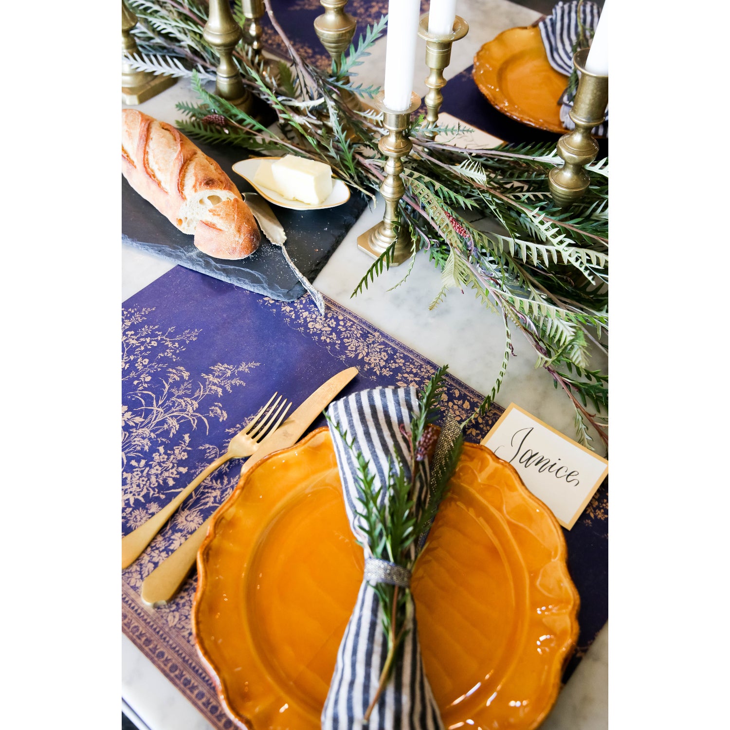 A floral-themed table setting with plates, napkins, silverware, and a Hester &amp; Cook Navy Woven Floral Placemat.