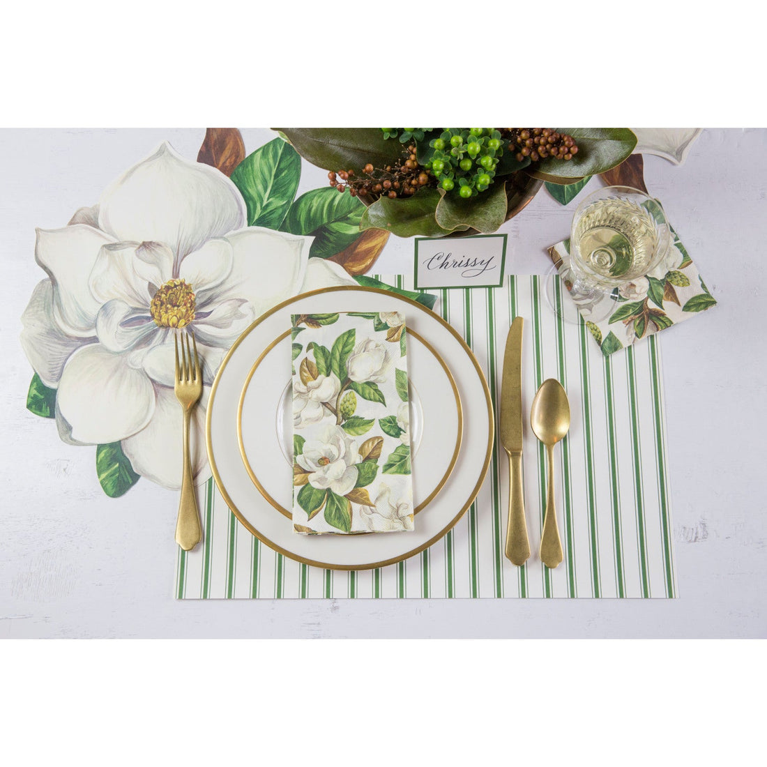 An elegant floral place setting with a Magnolia Guest Napkin centered on the plate, and a Magnolia Cocktail Napkin under the glass of wine, from above.