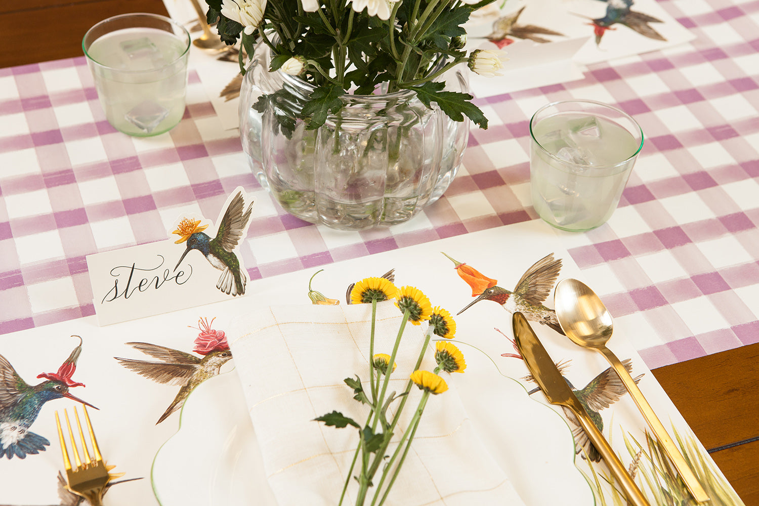 A table setting with flowers and hummingbirds adorned with a stunning Lilac Painted Check Runner by Hester &amp; Cook.