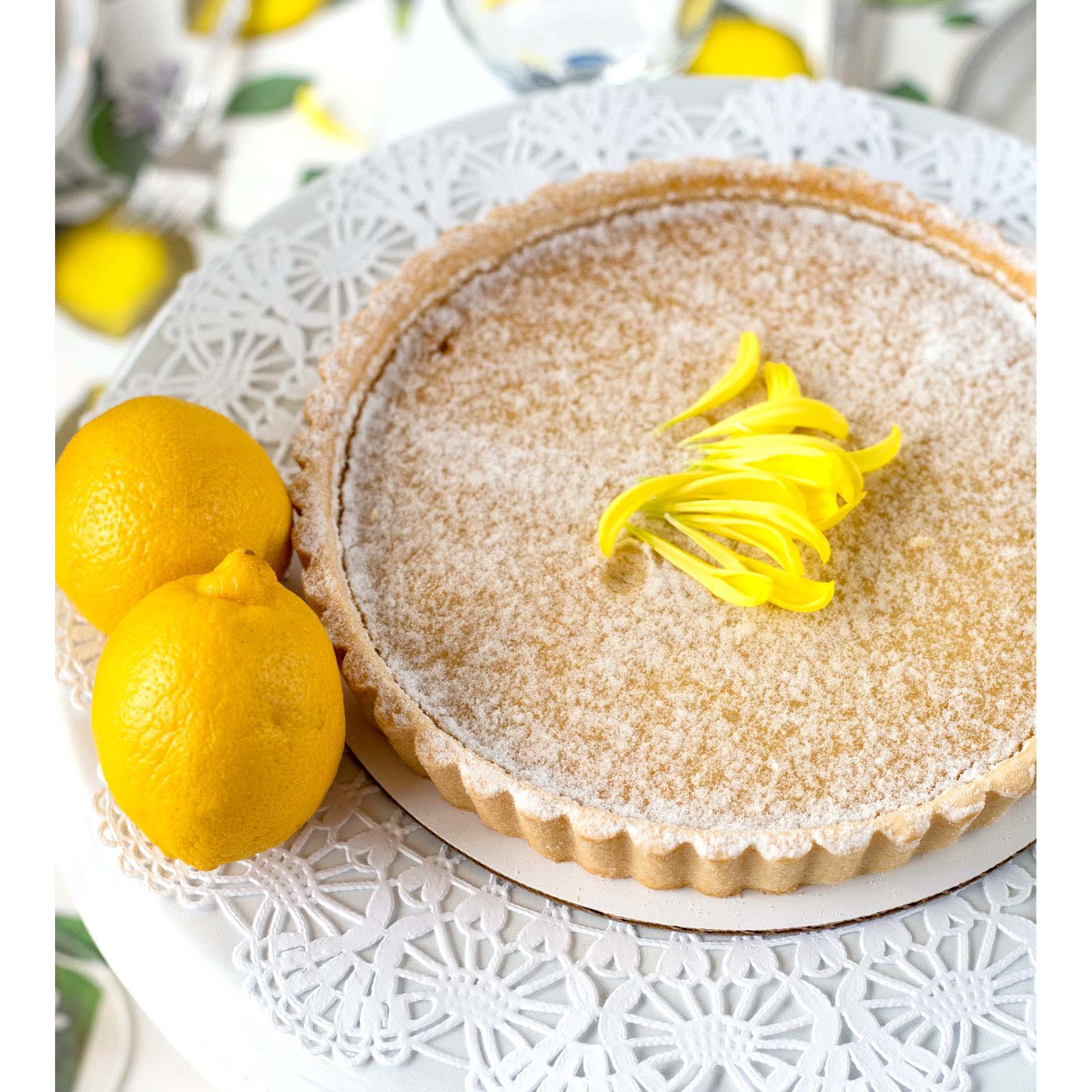 A beautiful lemon tart centered on a Doilie Serving paper on a cake riser.