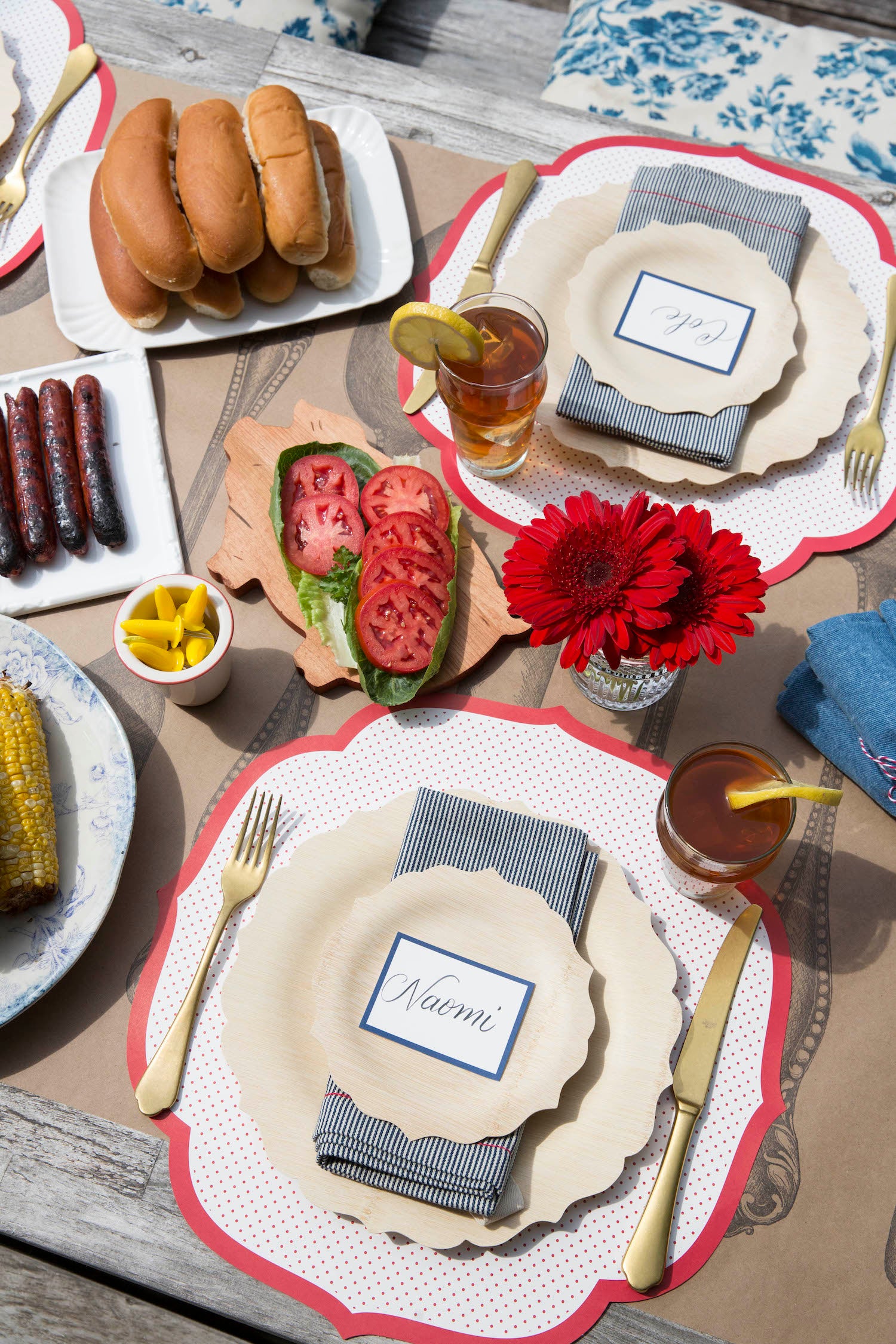 A tablescape featuring a Die-cut Red Swiss Dot Placemat from Hester &amp; Cook with a delectable hot dog and corn on the cob, representing a classic American dish.