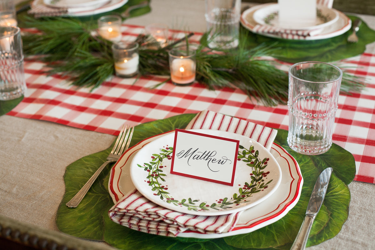 A special Christmas table setting with a Hester &amp; Cook Red Frame Place Card and a red and white checkered tablecloth for guests.