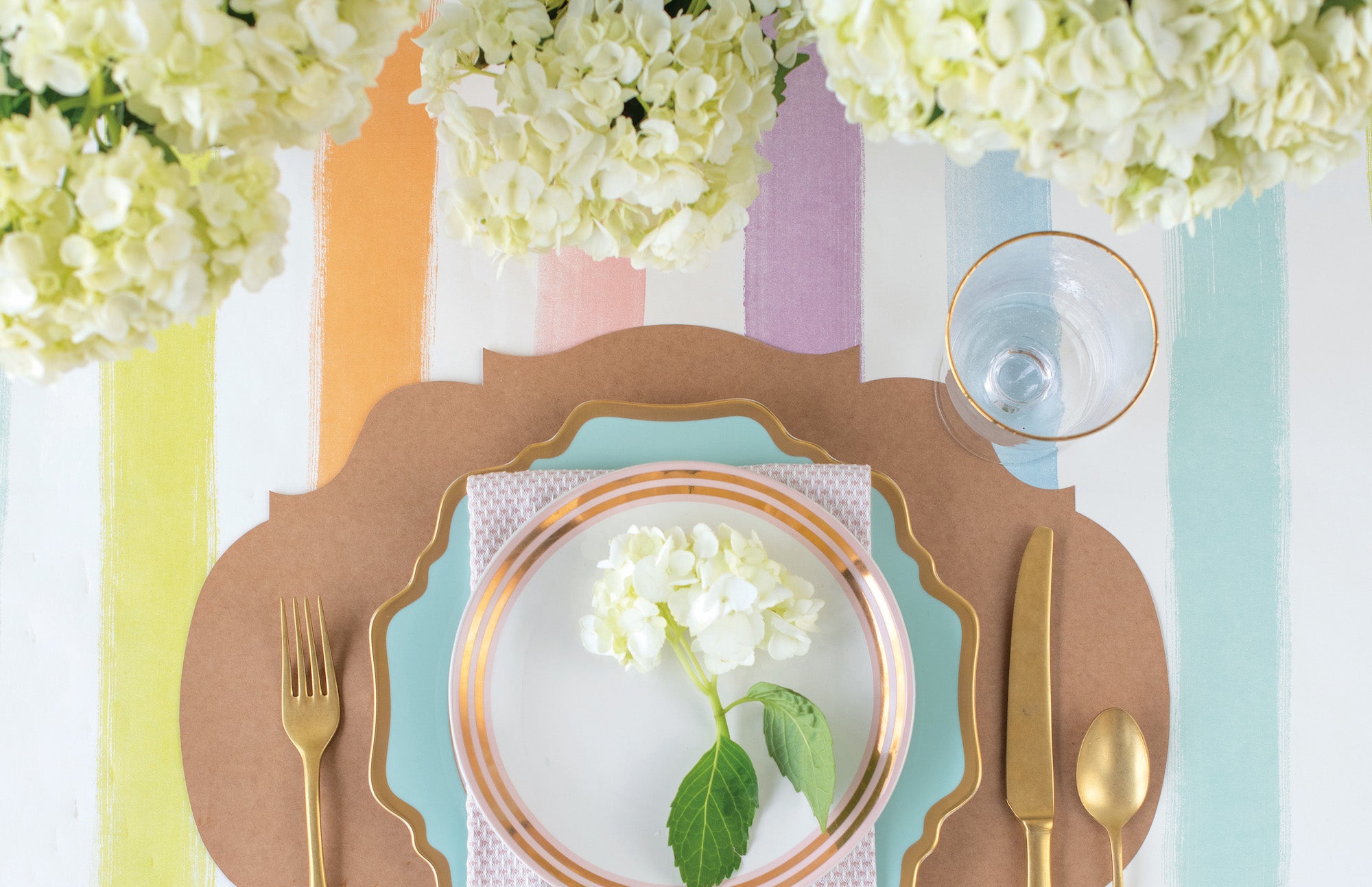 A luxurious table setting with an elegant Sorbet Painted Stripe Runner from Hester &amp; Cook, and a gleaming golden plate, perfect for entertaining guests.