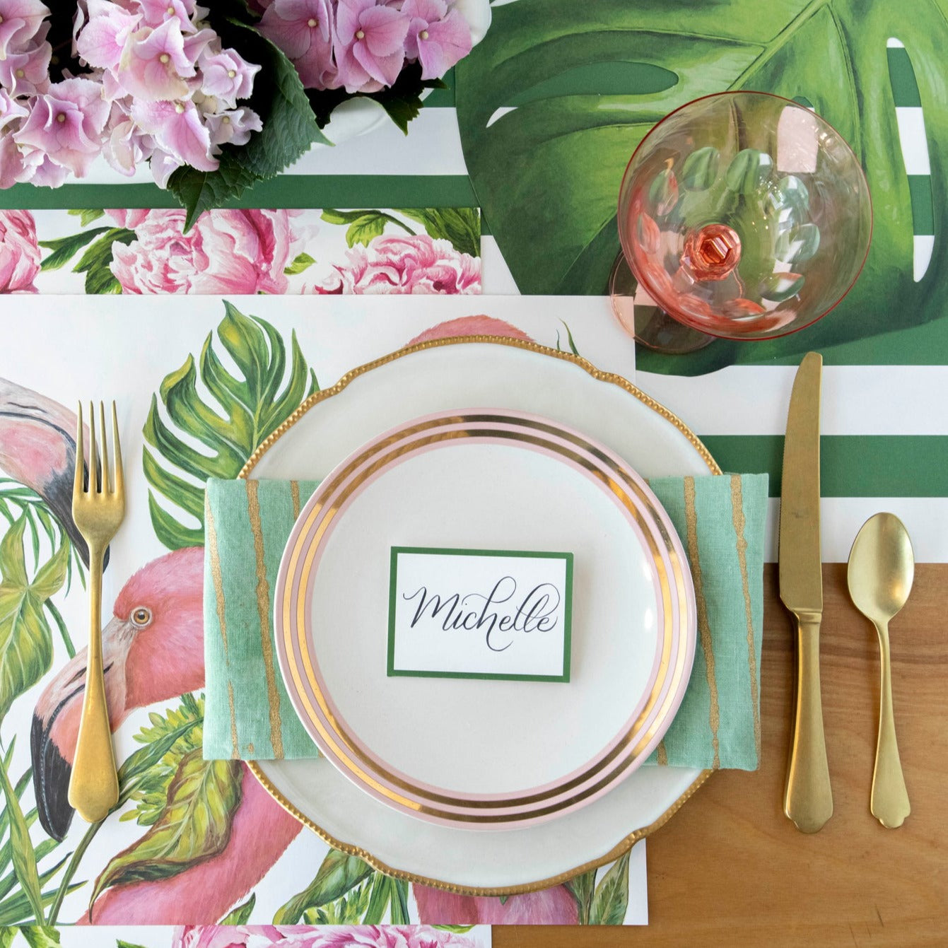 A table setting with an elegant touch of the Die-cut Monstera Placemat from Hester &amp; Cook, adorned with flamingos and flowers.