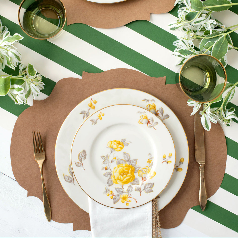 A tablescape set with Die-cut Kraft French Frame Placemat by Hester &amp; Cook, plates, silverware, and napkins on a green and white striped tablecloth.
