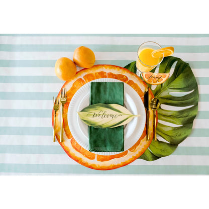 An elegant table setting with oranges, lemons and limes on a striped tablecloth, adorned with Die-cut Monstera Placemat by Hester &amp; Cook.