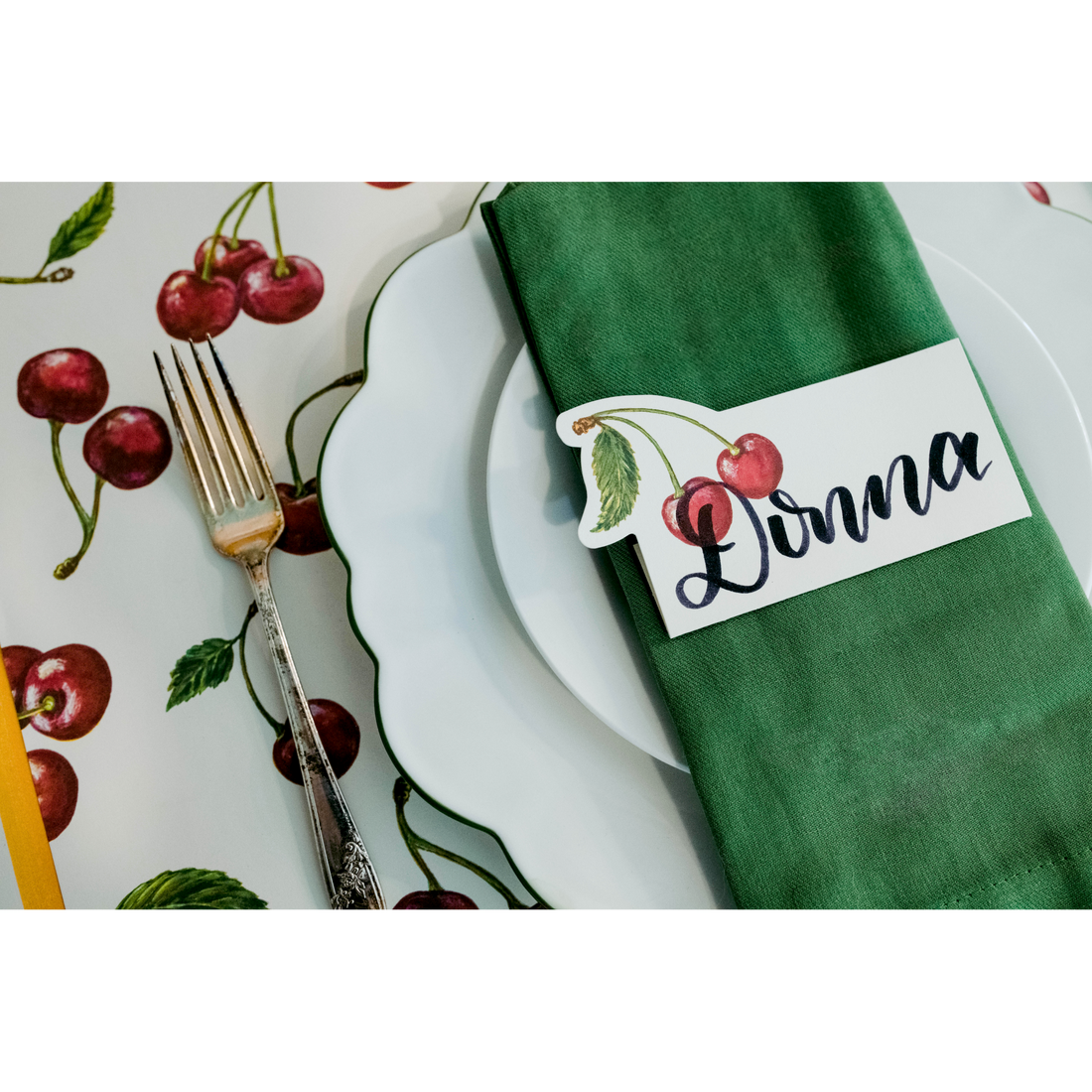 An elegant place setting featuring a Cherries Place Card reading &quot;Donna&quot; laying flat on the napkin over the plate.