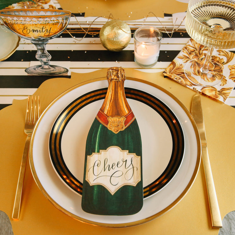 An elegant place setting featuring a Champagne Table Accent with &quot;Cheers&quot; written on the label in cursive.