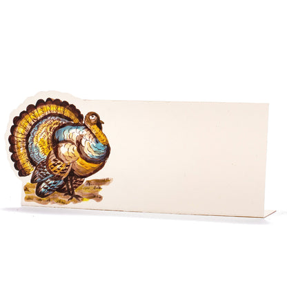 A white, rectangular freestanding place card featuring an illustrated turkey in brown, yellow and blue adorning the left side of the card.