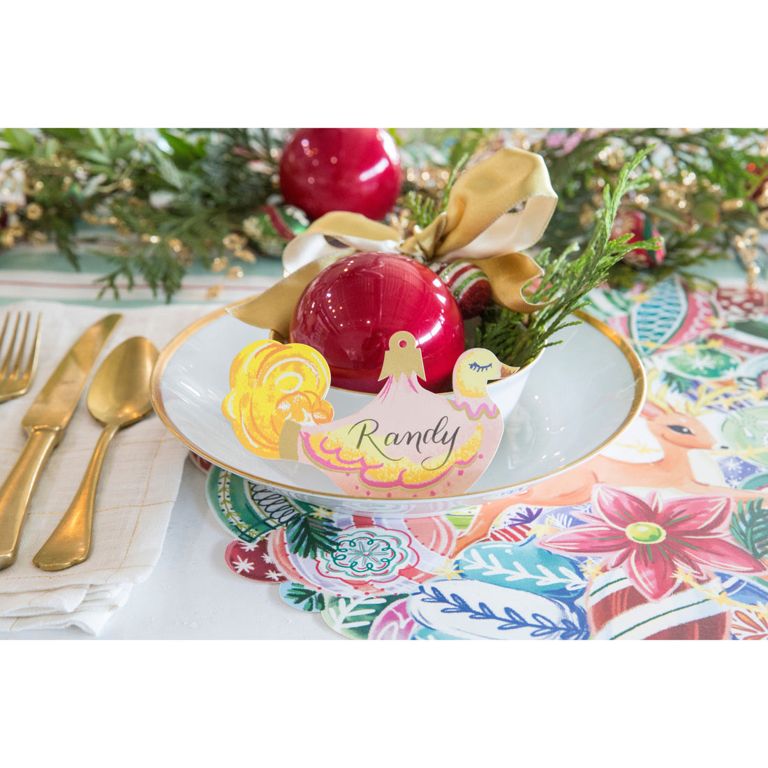A vintage-style Christmas place setting featuring a Swan Ornament Place Card labeled "Randy" standing on the plate.