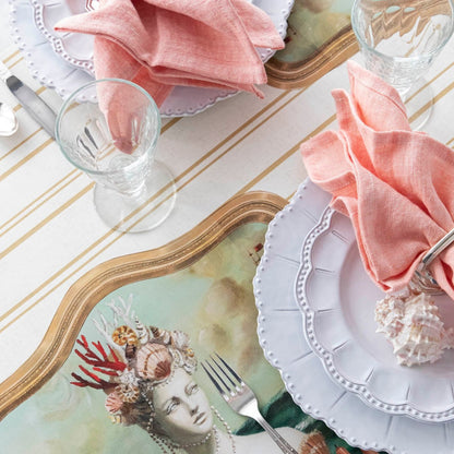 A table setting with plates, napkins, and a picture of a mermaid adorned with an Hester &amp; Cook Antique Gold Stripe Runner.