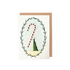 The Candy Cane Greeting Card features an illustration of a woman in a long green dress holding a gigantic red and white candy cane within a frame of green foliage, with a brown kraft paper envelope included.