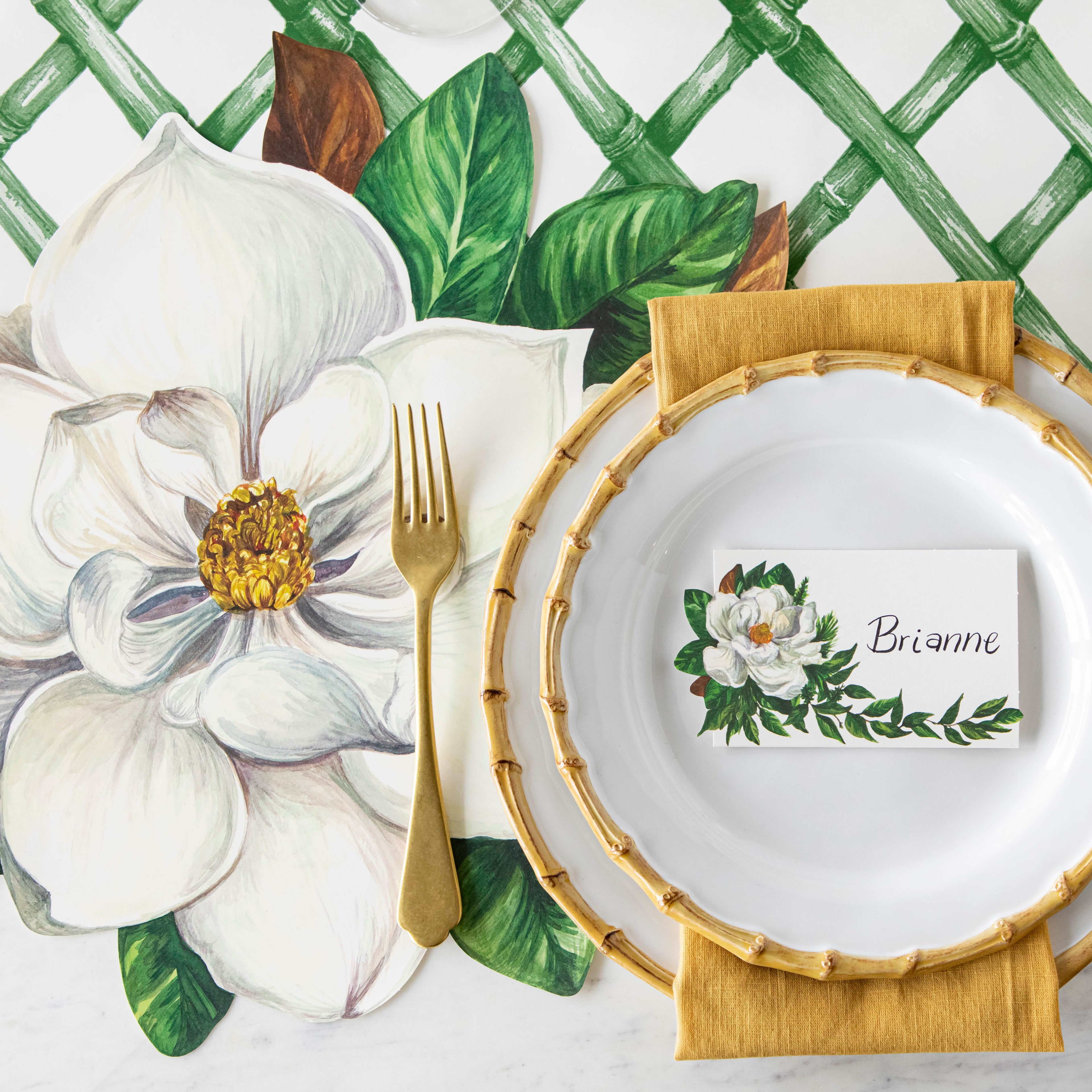 Top-down view of an elegant place setting featuring a Magnolia Place Card labeled &quot;Brianne&quot; laying flat on the plate.