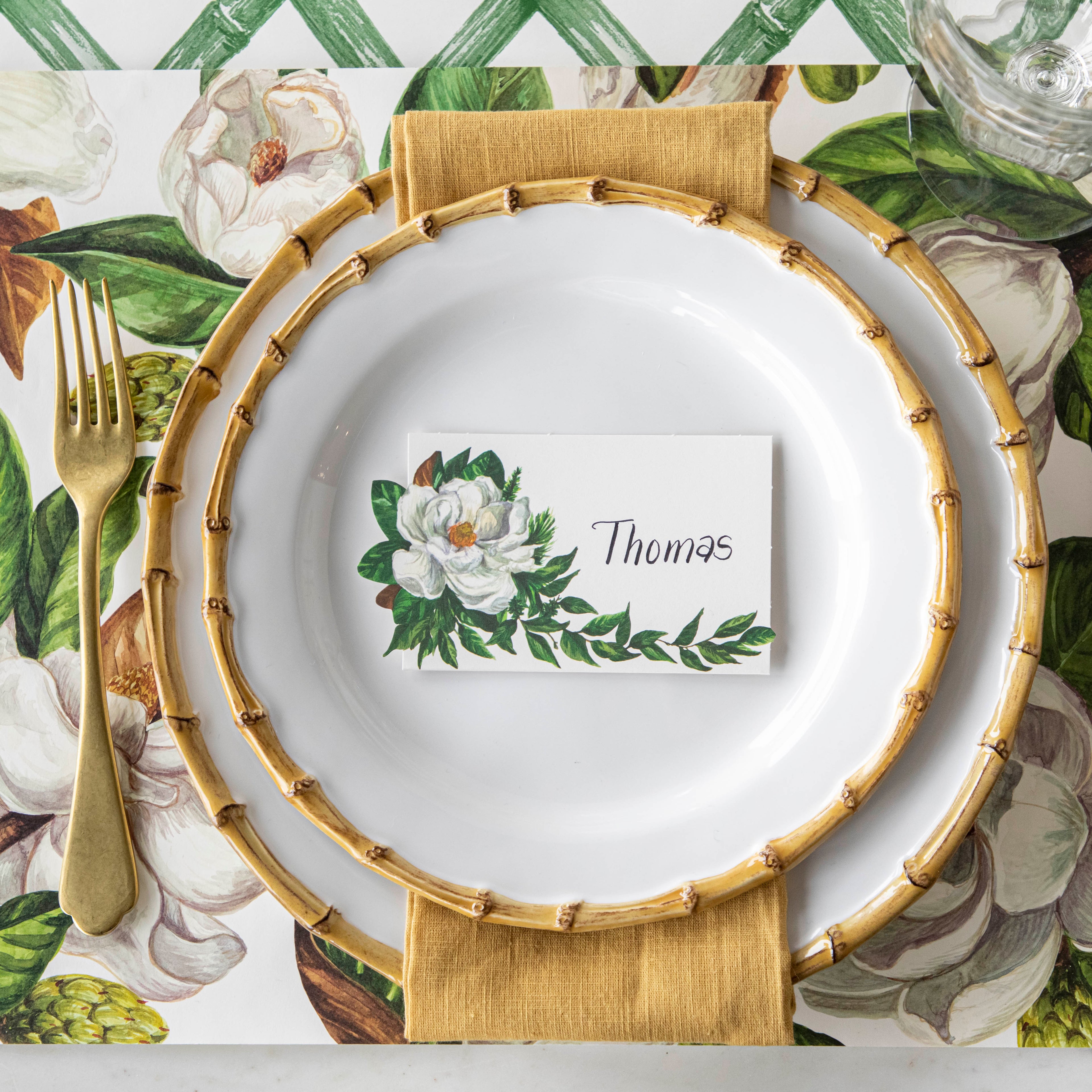 Top-down view of an elegant place setting featuring a Magnolia Place Card labeled &quot;Thomas&quot; laying flat on the plate.