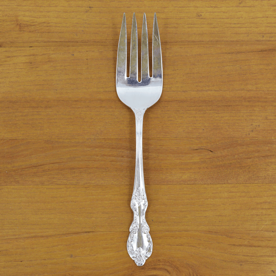 A Hester &amp; Cook vintage silver-plate meat fork resting on a folded green napkin with pom-pom trim on a marble countertop.