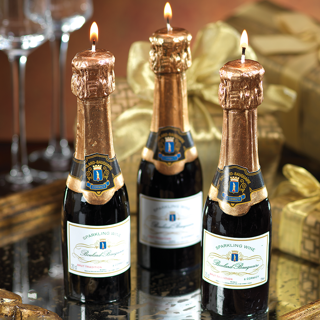 Three Zodax Mini Champagne Bottle Candles with lit candles on top, set against a celebratory backdrop as part of an elegant event table setting.