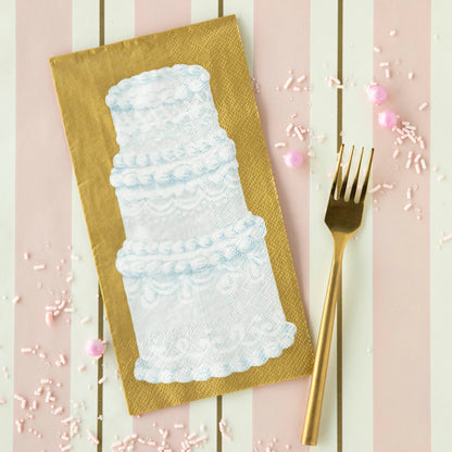A Tiered Cake Guest Napkin on a pink table runner with a gold fork.