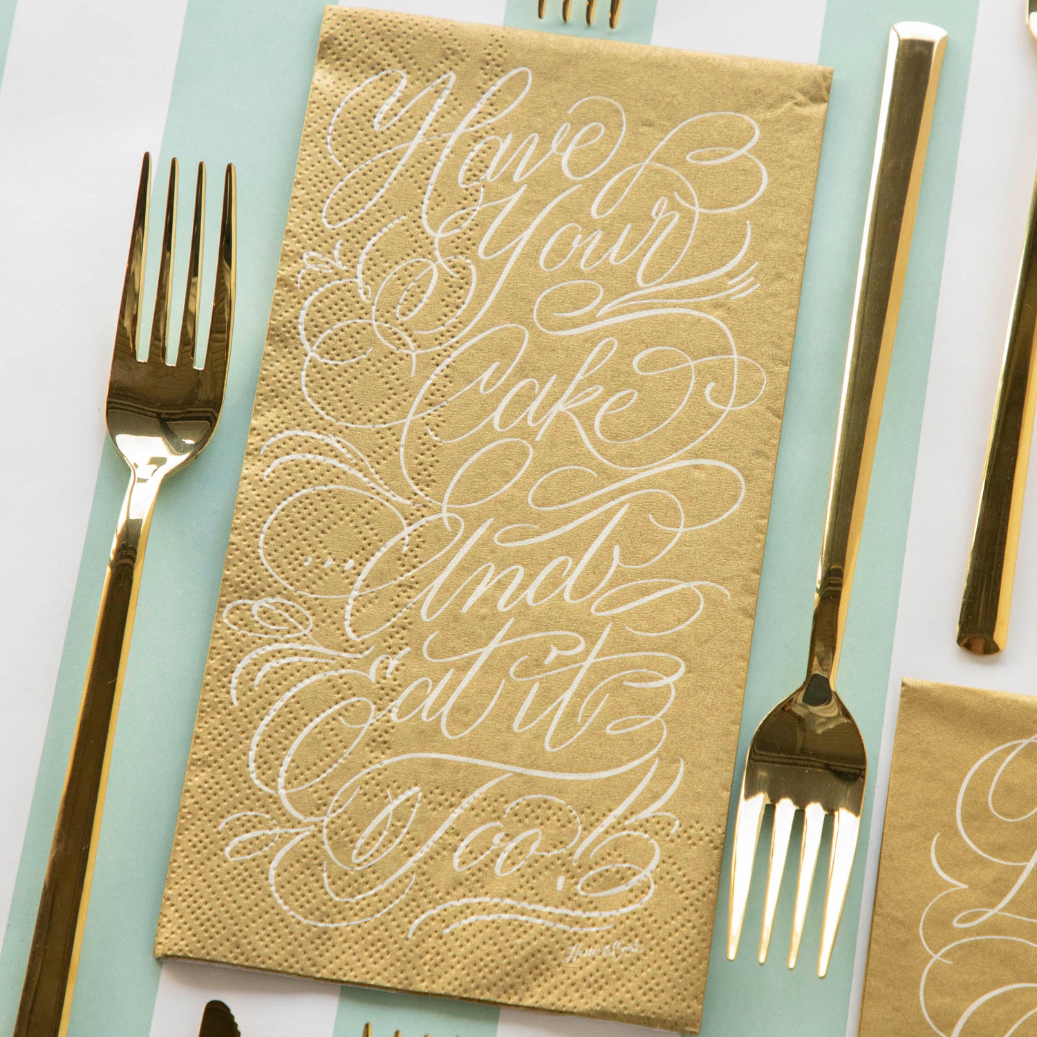 A Cake Guest Napkin on a striped table runner with gold cutlery.