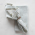 A durable, Bergen Green Napkin by Taylor Linen with blue and white stripes on a white surface.