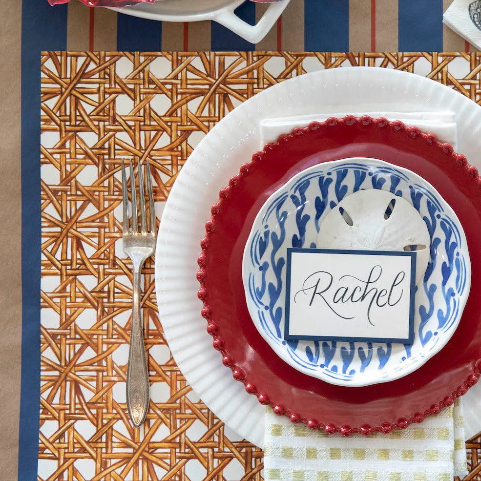 A table setting with red, white, and blue plates and silverware arranged on a Hester &amp; Cook Rattan Weave placemat.