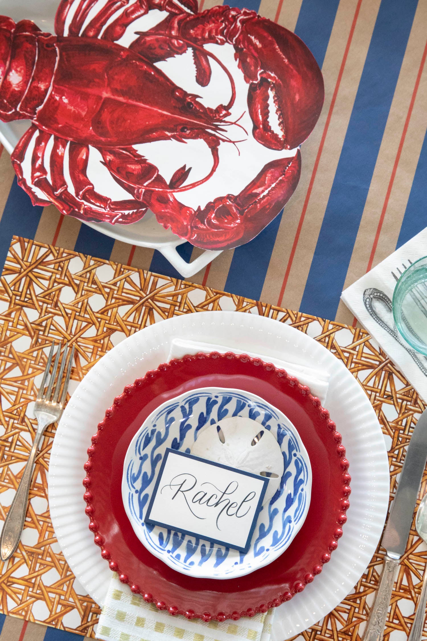 The Die-cut Lobster Placemat resting on a serving dish in an elegant place setting, from above.
