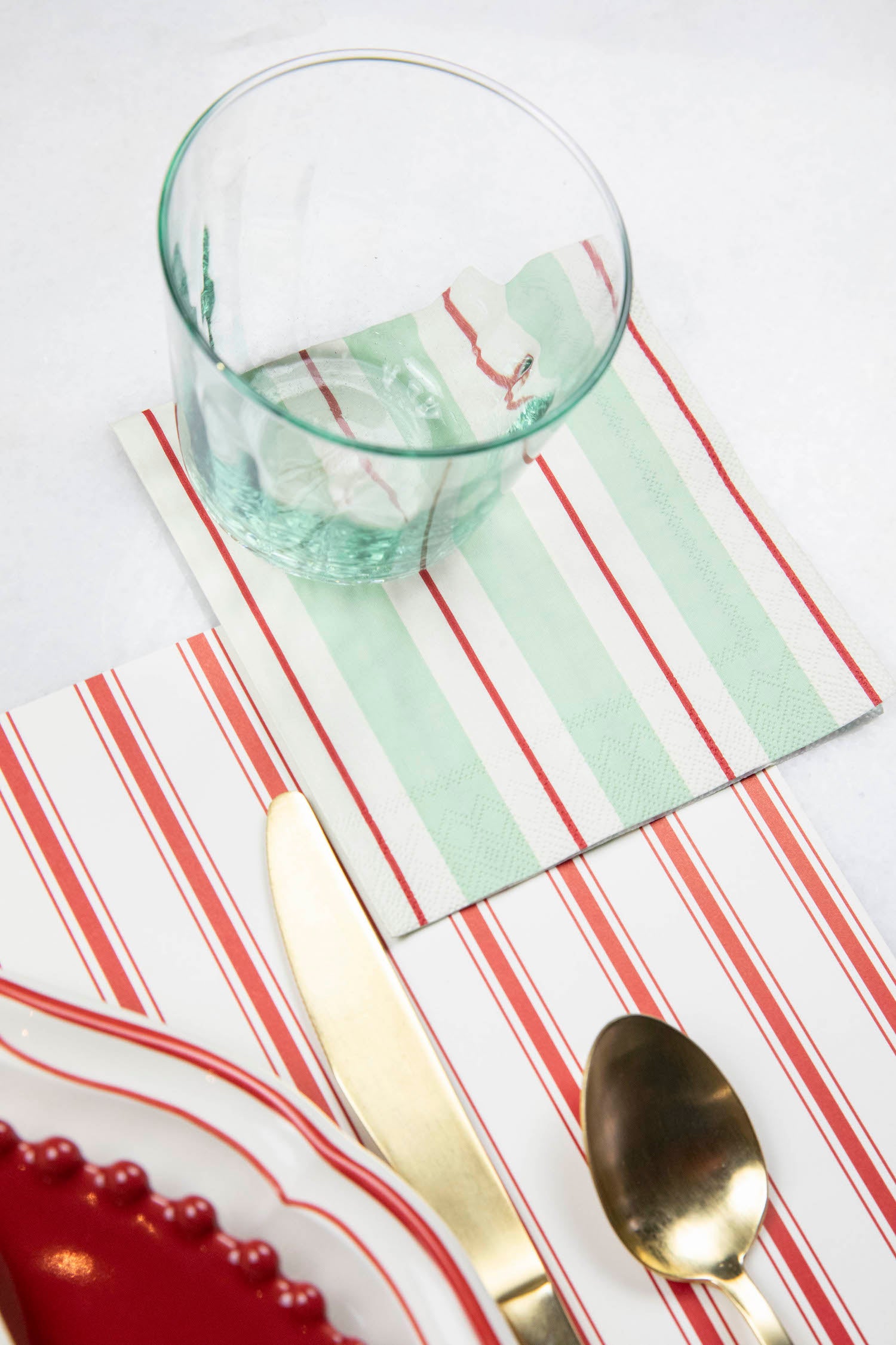 A Seafoam &amp; Red Awning Stripe Cocktail Napkin in an elegant place setting.