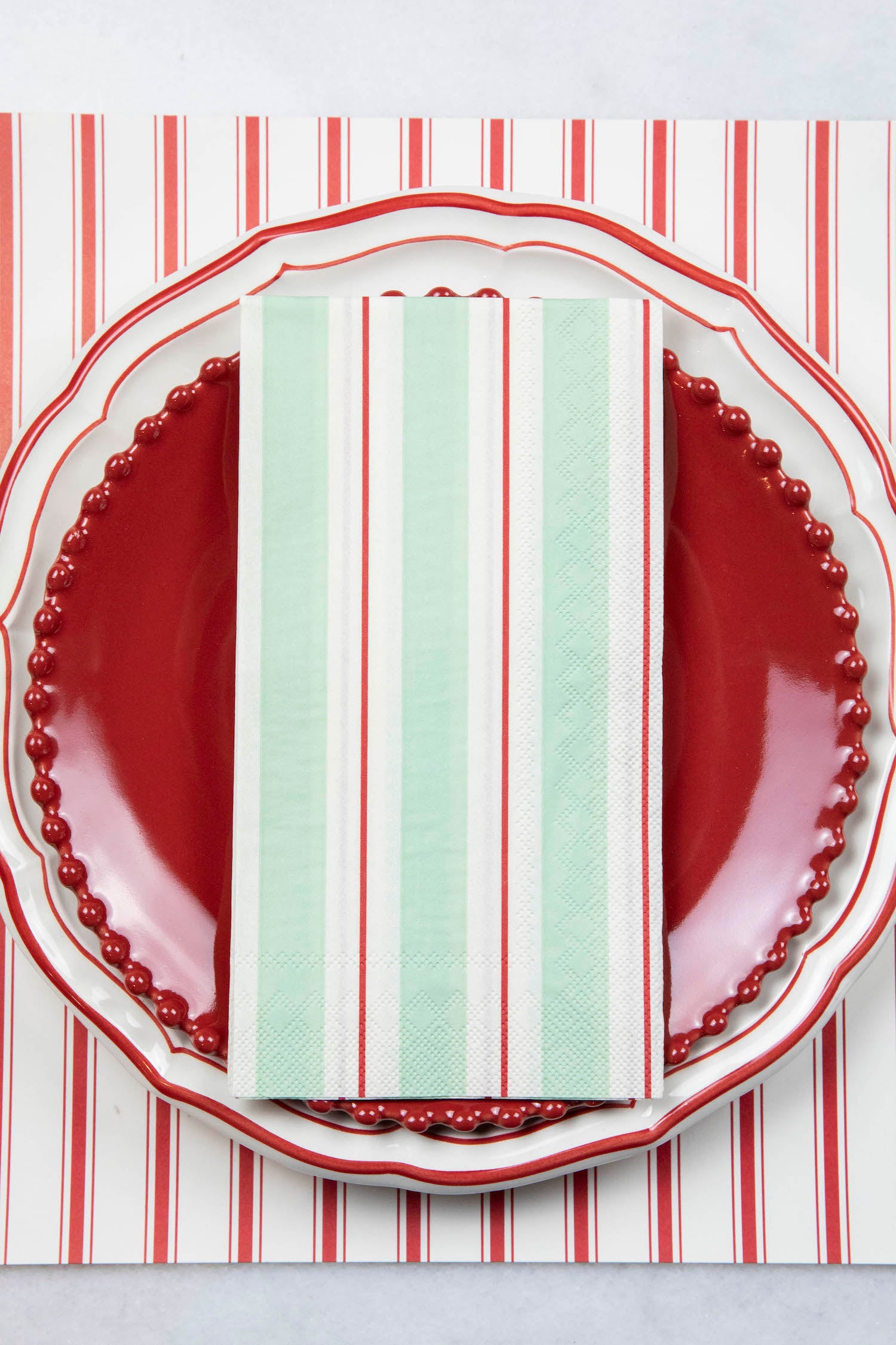A Seafoam &amp; Red Awning Stripe Guest Napkin centered on the plate of a place setting.
