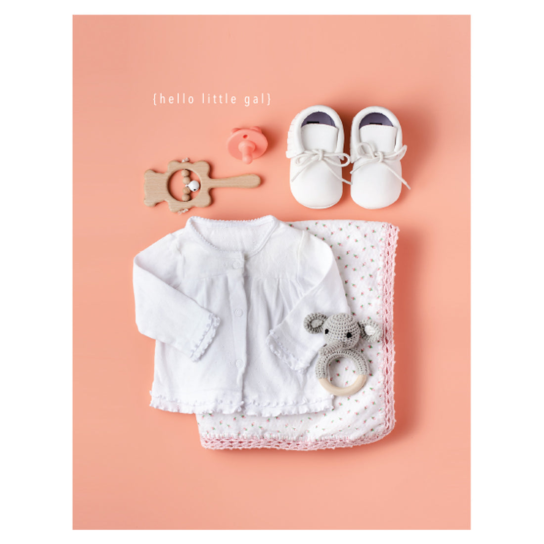 A photo of white and pink baby items including a shirt, folded blanket, shoes, a rattle and a pacifier on a pink background, with &quot;{hello little gal}&quot; printed in white above the toys.