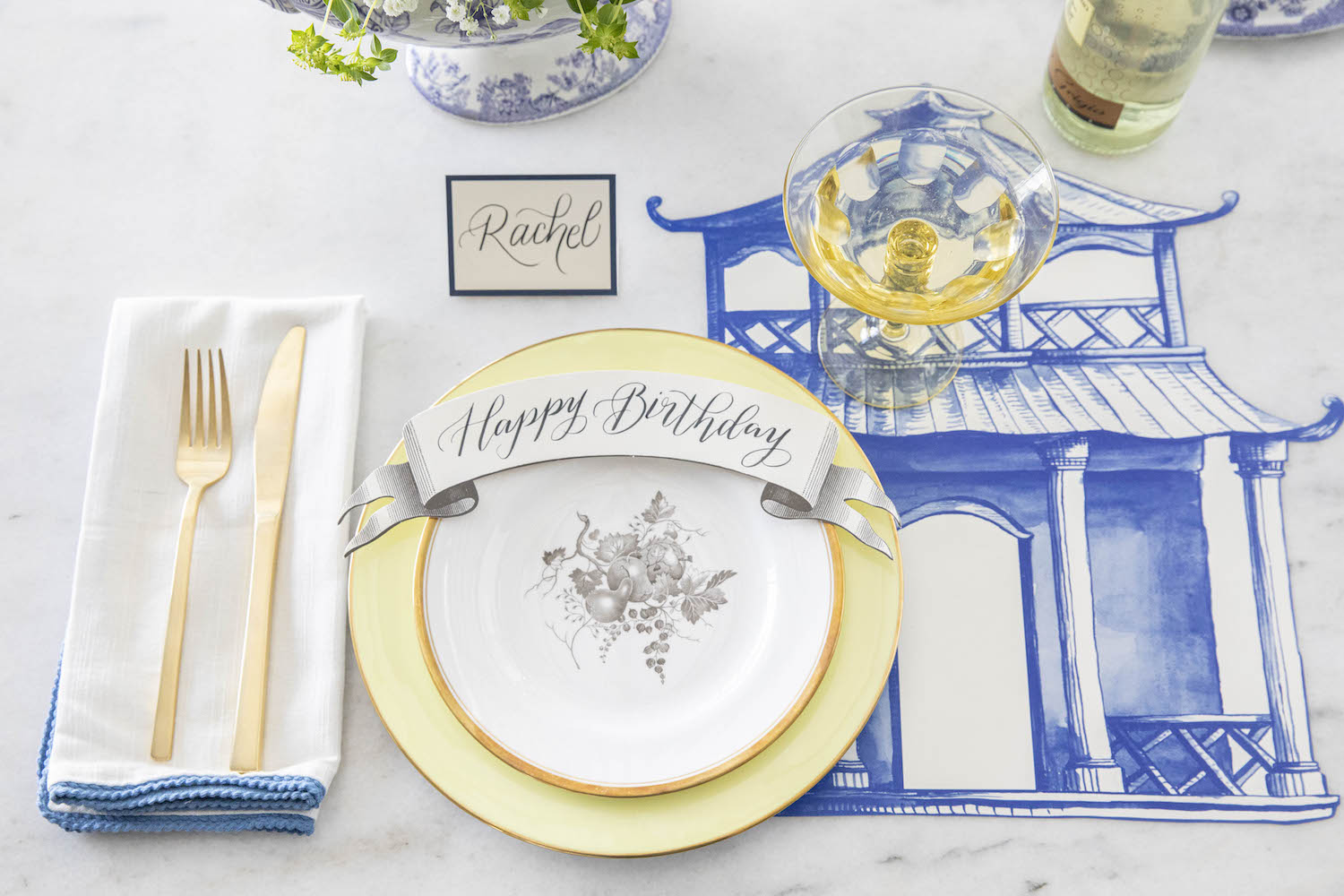An elegant blue and white tablescape adorned with a Die-cut Pagoda Placemats from Hester &amp; Cook, along with a happy birthday sign and paper placemats.