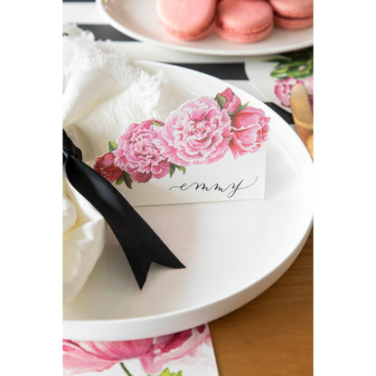 An elegant place setting featuring a Peony Place Card labeled &quot;Emmy&quot; standing on the plate.