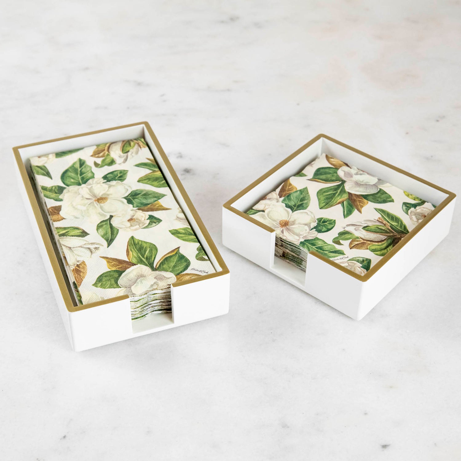 A lacquered wood holder for beverage and guest napkins, featuring a white color with gold trim and a floral pattern napkin inside.