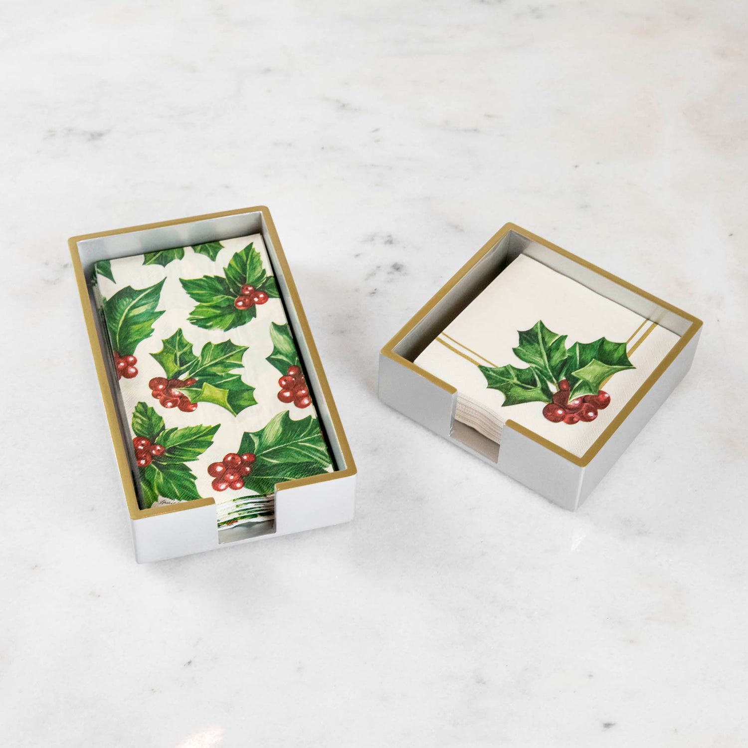 A silver colored lacquered napkin holder in guest and cocktail size with napkins in them. 