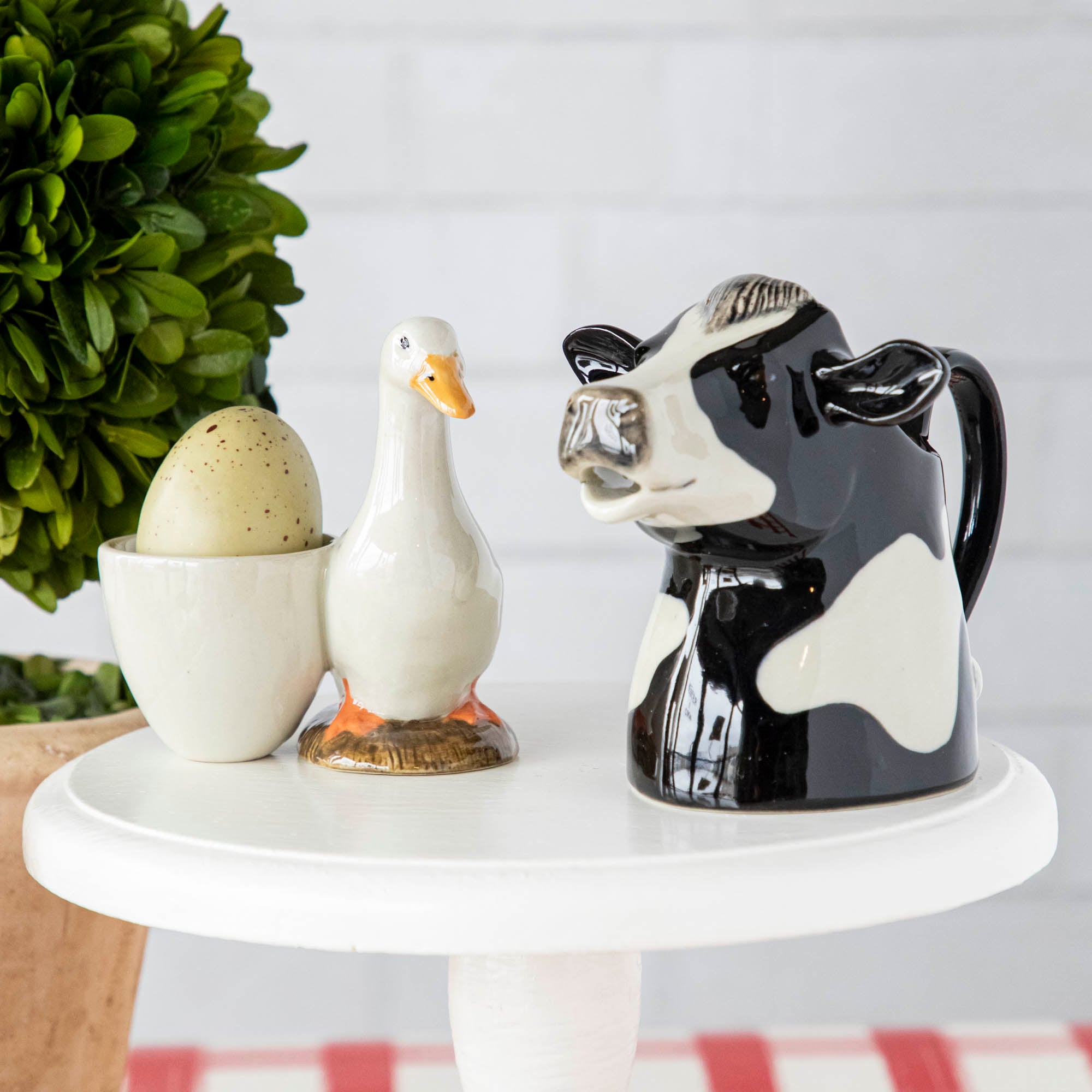 A black and white cow jug and a duck, two quirky pieces by Farm Animal Ceramics, a Quail brand, placed on a table.
