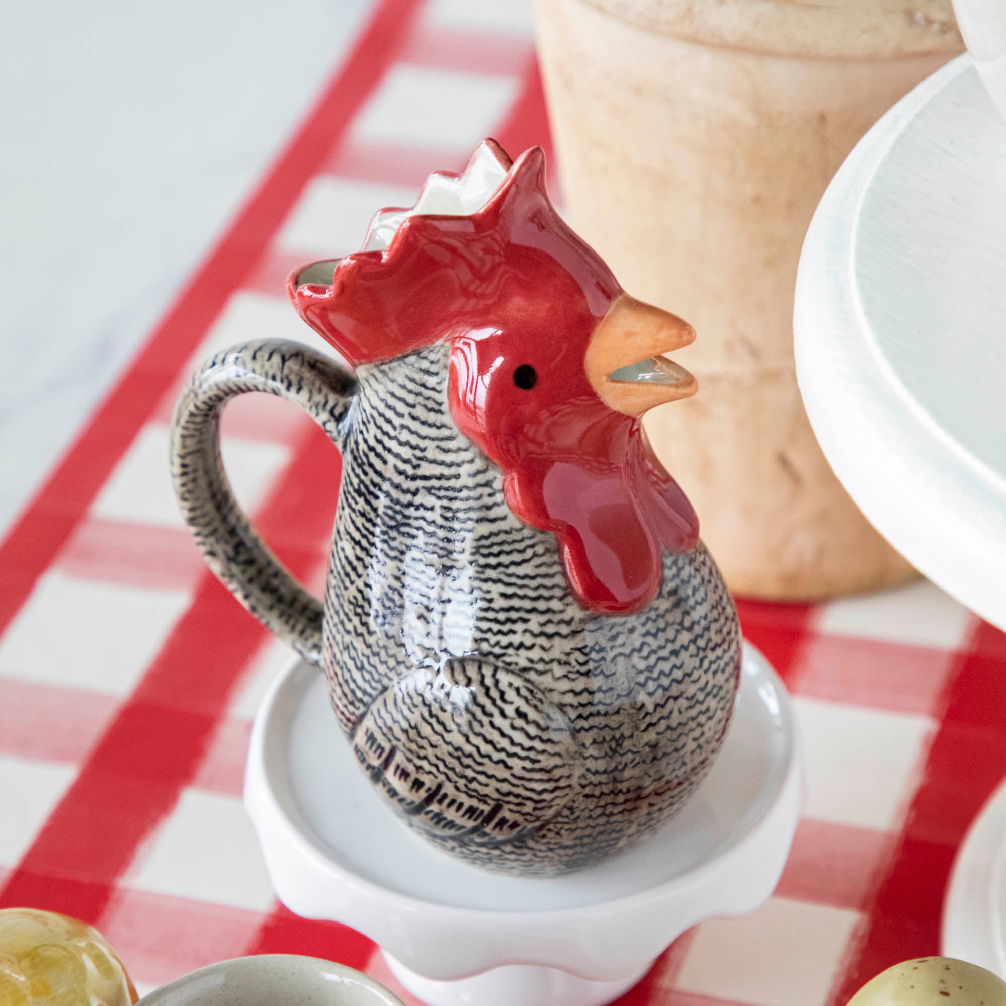 A Farm Animal Ceramics ceramic rooster sits on a red and white checkered table.
