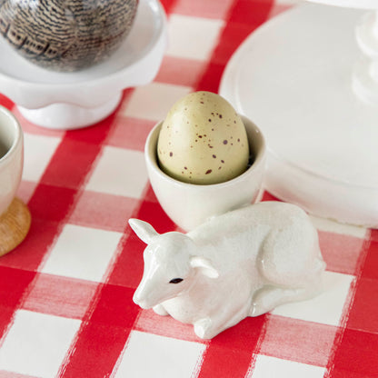 A red and white checkered tablecloth adorned with a quirky cow figurine from Quail Ceramics, a British brand known for their unique Farm Animal Ceramics pieces.