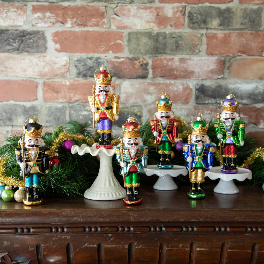 Glass Glitterville Nutcracker Ornaments on a mantle with Christmas decorations.