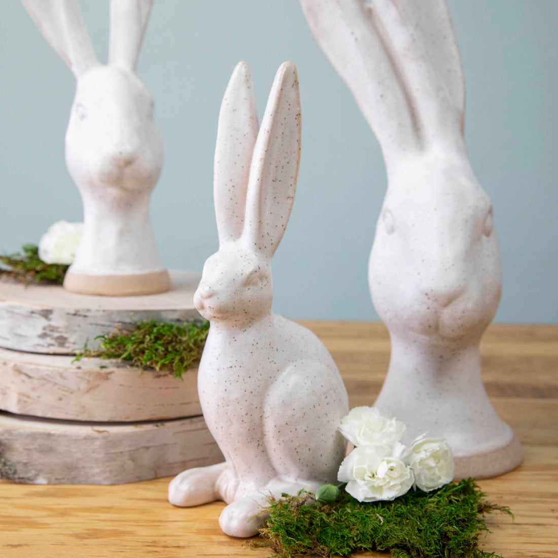 A group of enchanting Matte White Ceramic Hares by HomArt, on a wood surface, serving as a garden decoration.