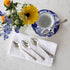 An elegant tea setting with an empty teacup and saucer, a Hester & Cook Vintage Silver-Plate Tea Spoon Set of Four, and a bouquet of fresh flowers on a marble surface.