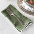 A Hester & Cook vintage silver-plate meat fork resting on a folded green napkin with pom-pom trim on a marble countertop.
