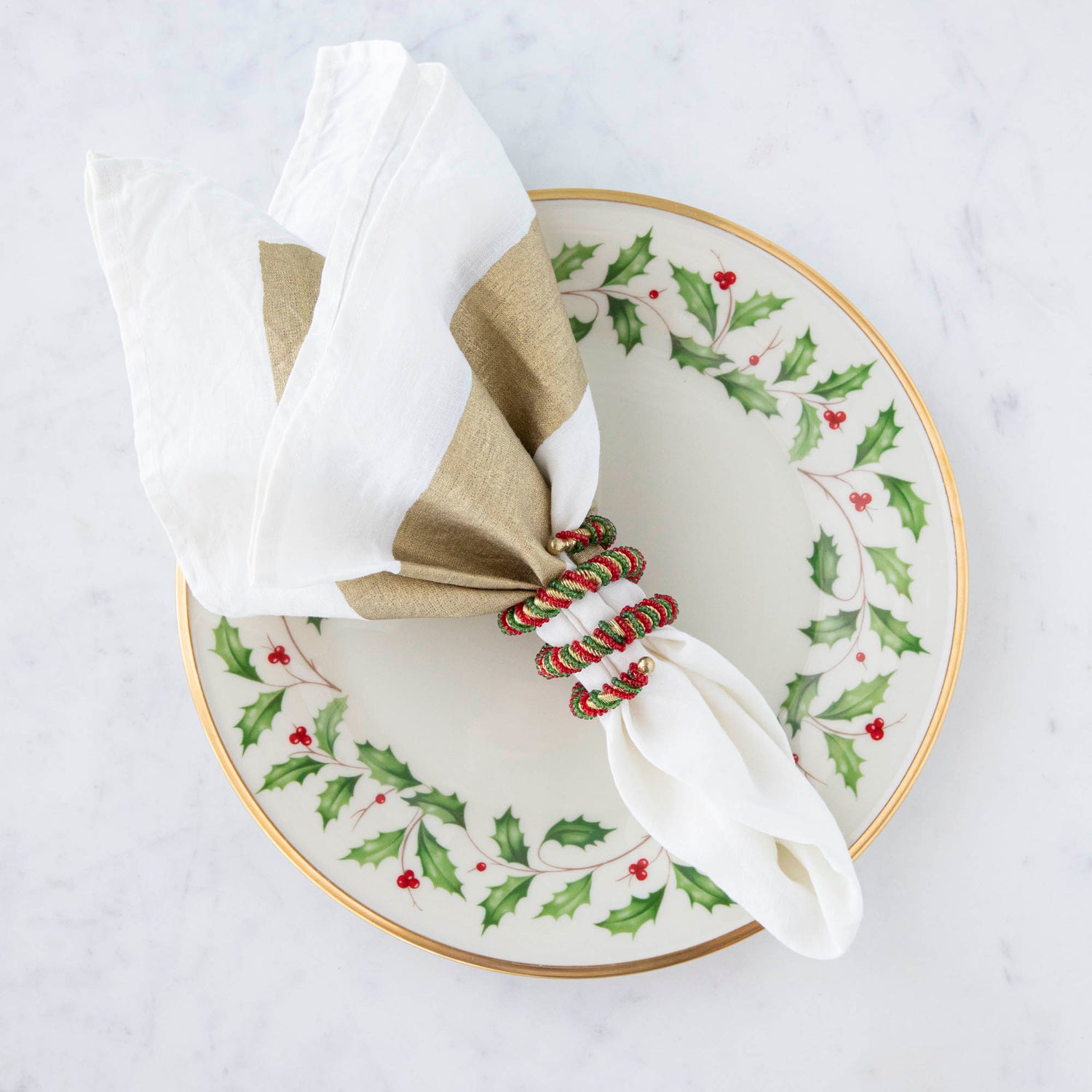A spiral napkin ring with red, green, and white colors, placed on a white napkin with a Christmas-themed pattern in the background.