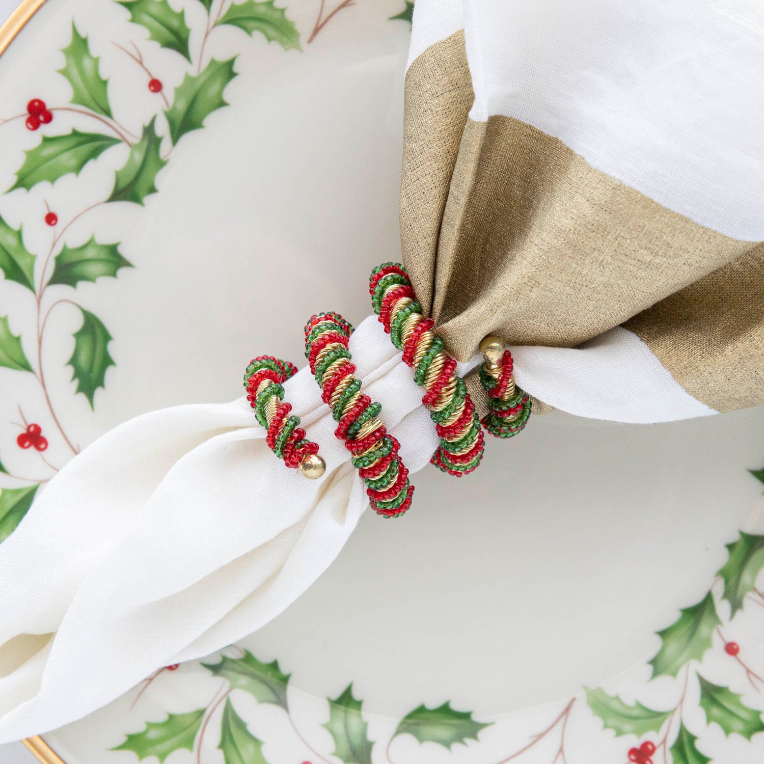 A spiral napkin ring with red, green, and white colors, placed on a white napkin with a Christmas-themed pattern in the background.