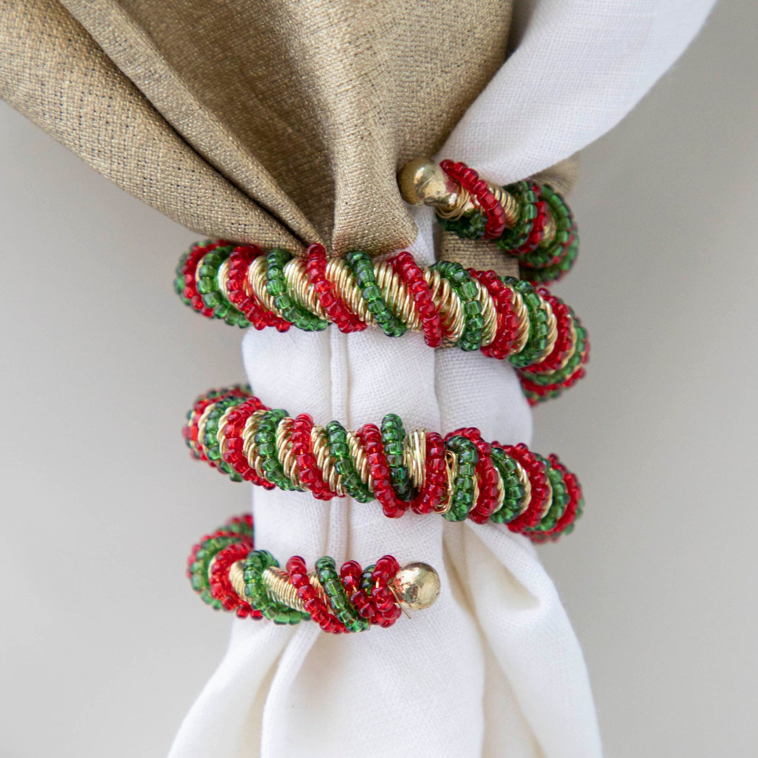 A spiral napkin ring with red, green, and white colors, placed on a white napkin with a Christmas-themed pattern in the background.