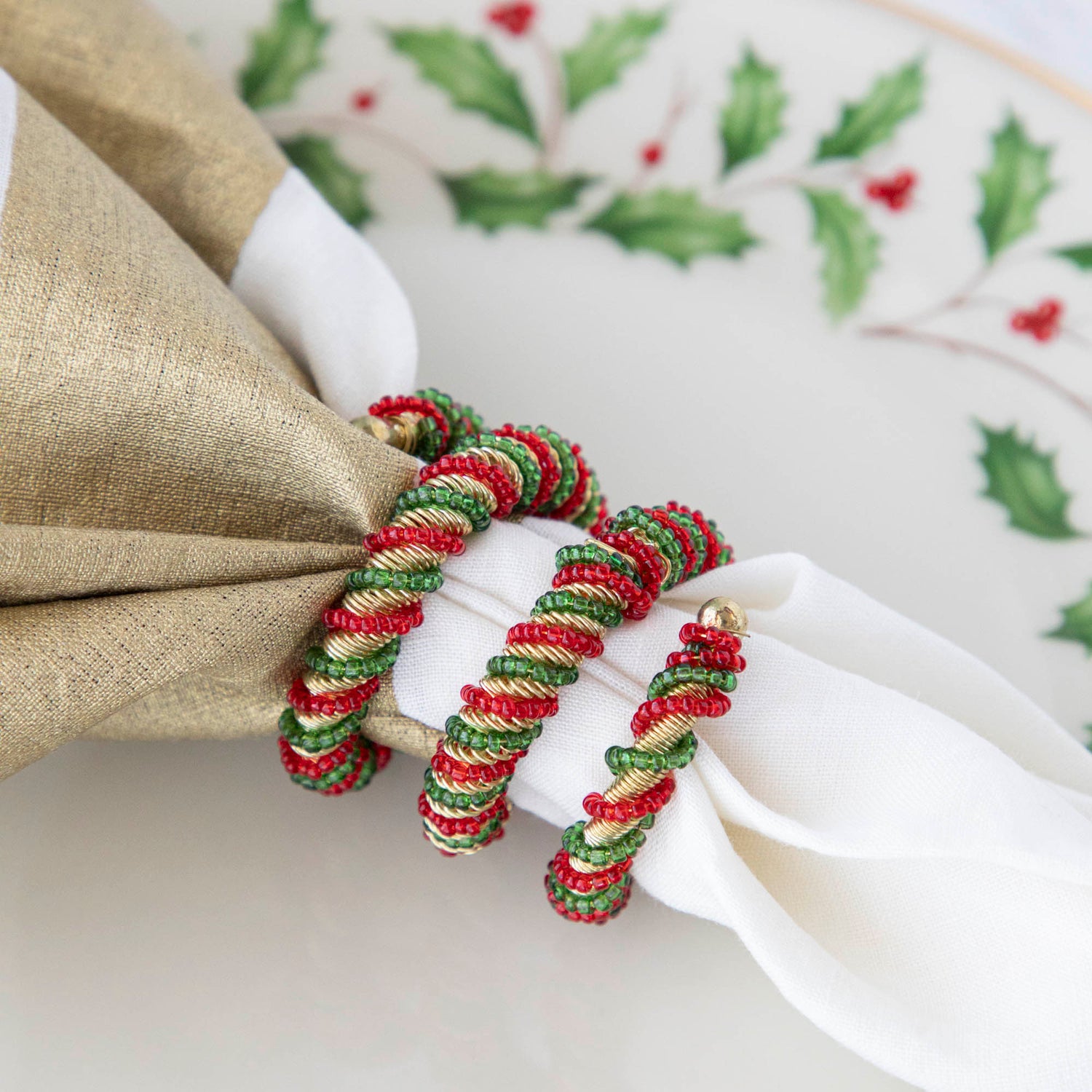 A spiral napkin ring with red, green, and white colors, placed on a white napkin with a Christmas-themed pattern in the background.