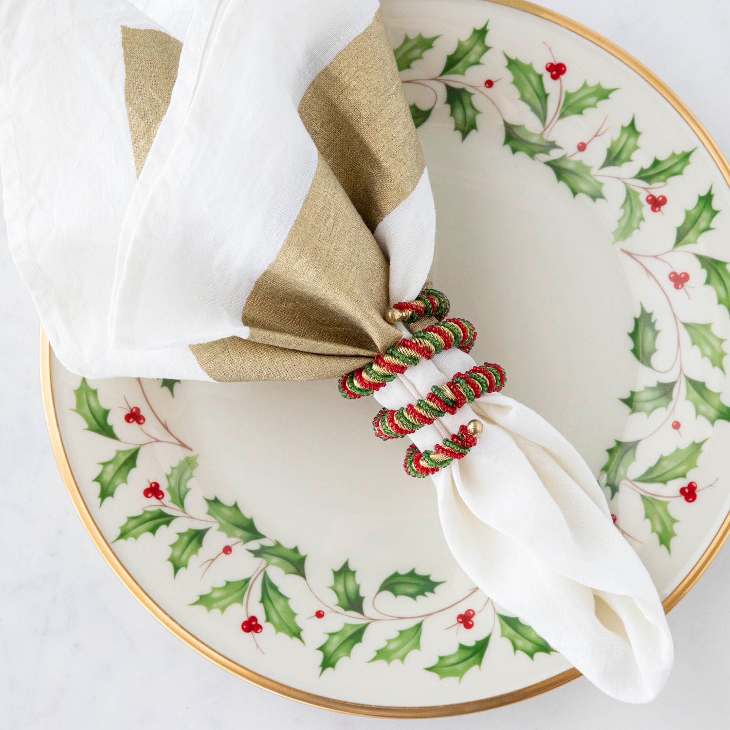 A spiral napkin ring with red, green, and white colors, placed on a white napkin with a Christmas-themed pattern in the background.